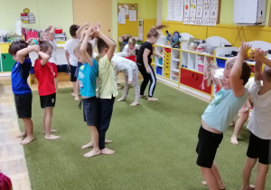 Dzieci, stojąc do siebie tyłem w parach, podają sobie piłeczkę nad głową i pomiędzy nogami